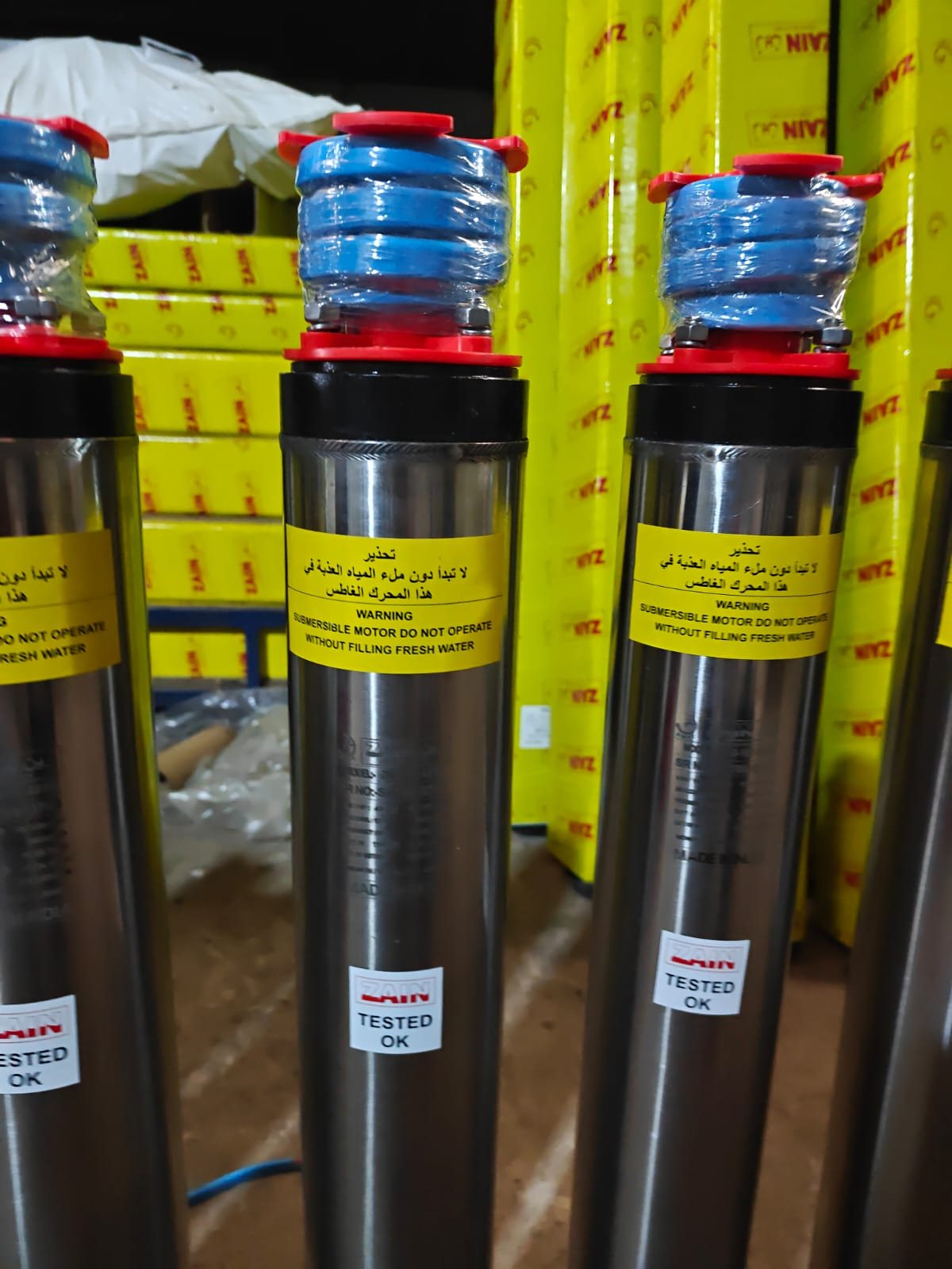 Three Zain stainless steel submersible motors with bilingual Arabic and English warning labels
